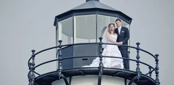 A bride and groom standing on the balcony of a lighthouse.