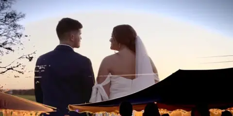 A bride and groom standing together at an outdoor wedding reception during sunset.