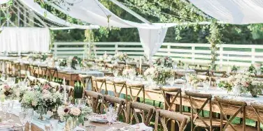 An outdoor wedding reception setup featuring long wooden tables, chairs, and a large white tent.