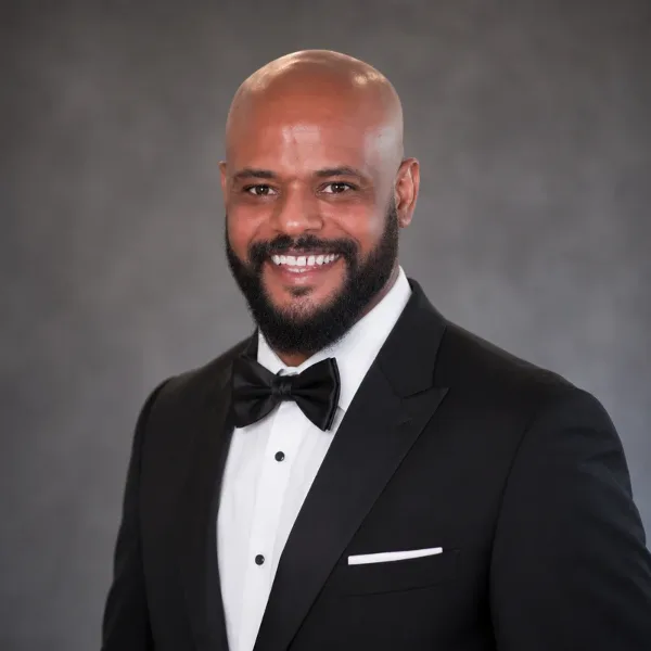 Portrait of a smiling man in a black tuxedo with bow tie, representing the taxi service driver.