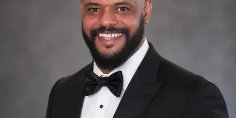 Portrait of a smiling man in a black tuxedo with bow tie, representing the taxi service driver.