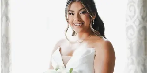 A smiling bride with styled hair and makeup holding a white rose bouquet.