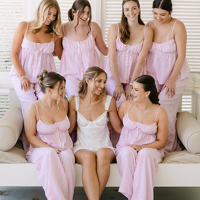 A bride and her bridesmaids in matching pink robes, posing together in a bright room.