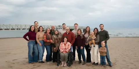 A large multi-generational family posing for a professional portrait on a sandy beach with a pier in the background.