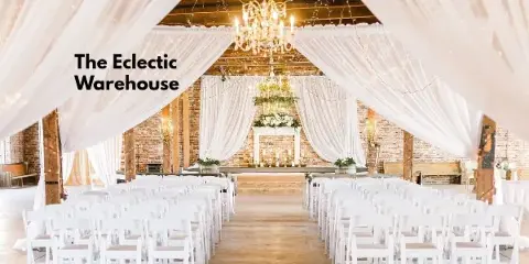 A wedding ceremony setup in a rustic indoor venue featuring white chairs, a floral altar, and hanging chandeliers.