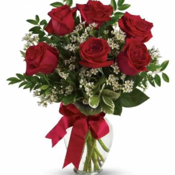 A bouquet of red roses with white filler flowers in a clear glass vase tied with a red ribbon.