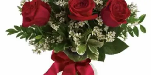 A bouquet of red roses with white filler flowers in a clear glass vase tied with a red ribbon.