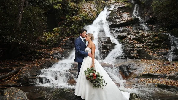 A bride and groom standing together in front of a rocky waterfall.