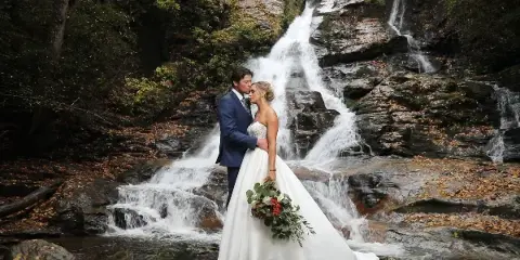 A bride and groom standing together in front of a rocky waterfall.