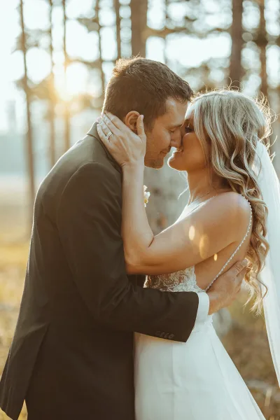 A bride and groom sharing an intimate moment in a sunlit forest setting.