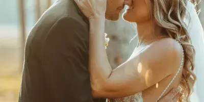 A bride and groom sharing an intimate moment in a sunlit forest setting.