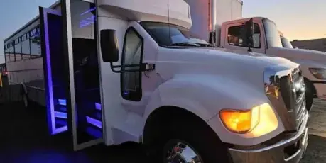 A white shuttle bus parked outdoors at dusk with its passenger door open, revealing blue LED lighting on the entry steps.