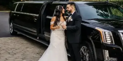 A bride and groom standing next to a black stretch limousine with the door open.