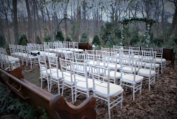 Rows of white Chiavari chairs arranged for an outdoor wedding ceremony with a floral arch in the background.