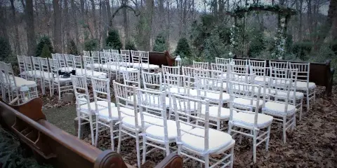 Rows of white Chiavari chairs arranged for an outdoor wedding ceremony with a floral arch in the background.