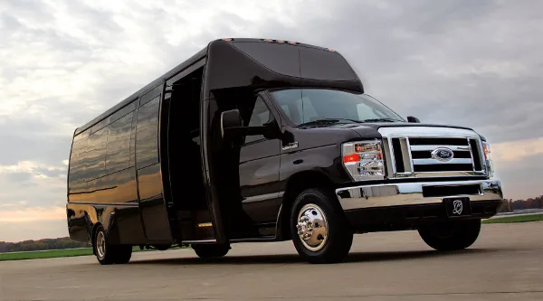 A black Ford E-Series shuttle van parked on a paved surface with its side door open.