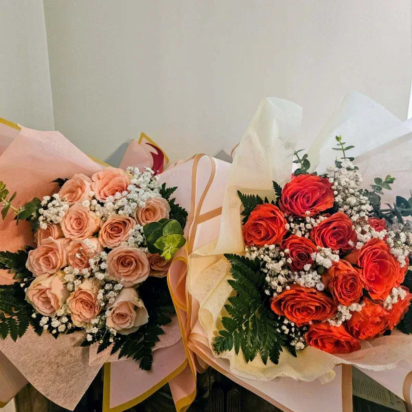 Two wrapped bouquets of roses, one in peach tones and one in orange, accented with baby's breath and greenery.