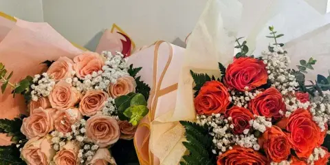 Two wrapped bouquets of roses, one in peach tones and one in orange, accented with baby's breath and greenery.