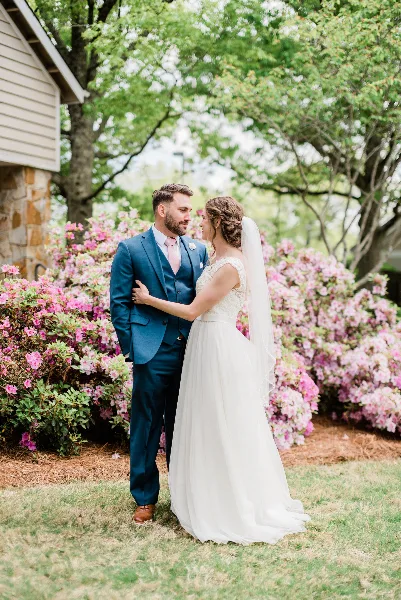 A bride and groom standing together outdoors in front of blooming pink flowers.