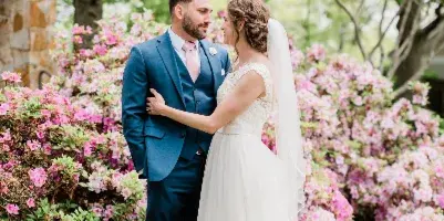 A bride and groom standing together outdoors in front of blooming pink flowers.