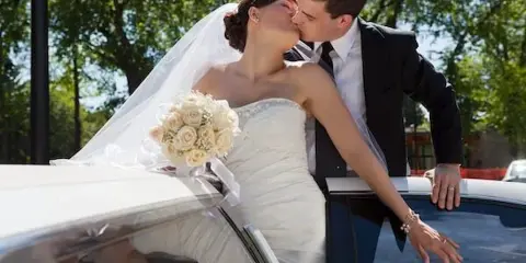 A bride and groom kissing next to a white limousine.