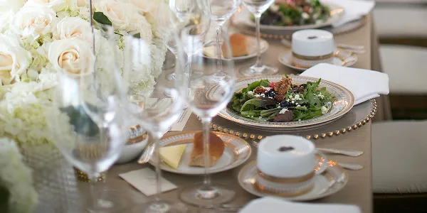 A close-up of an elegant wedding table setting featuring a plated salad, wine glasses, and white rose centerpieces.