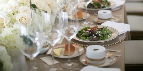 A close-up of an elegant wedding table setting featuring a plated salad, wine glasses, and white rose centerpieces.