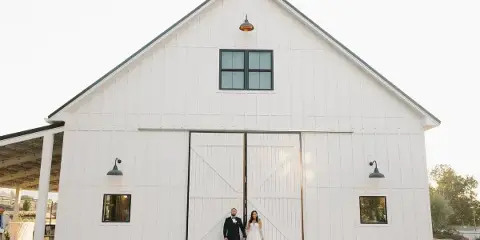 Exterior view of a large white barn with a couple standing in front of the main doors.