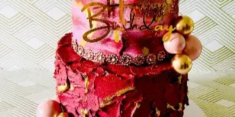 A two-tiered custom cake with red and pink frosting, gold leaf accents, and a 'Happy Birthday 50' topper.