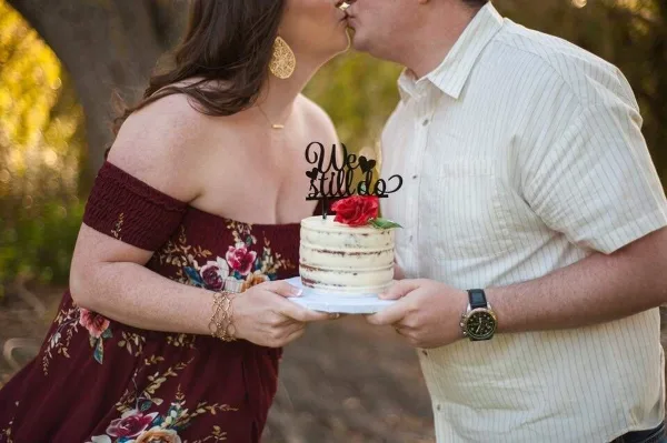 A couple holding a small, decorated cake with a 'We Still Do' topper.