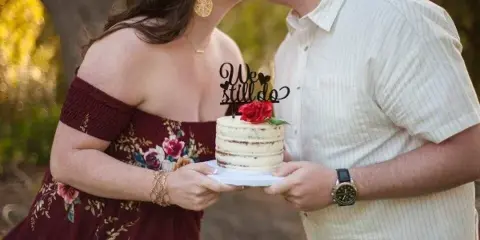 A couple holding a small, decorated cake with a 'We Still Do' topper.
