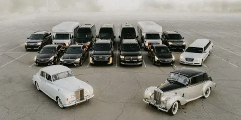 Aerial view of a luxury limousine fleet including vintage Rolls-Royce and Bentley cars, modern sedans, and SUVs parked in a lot.