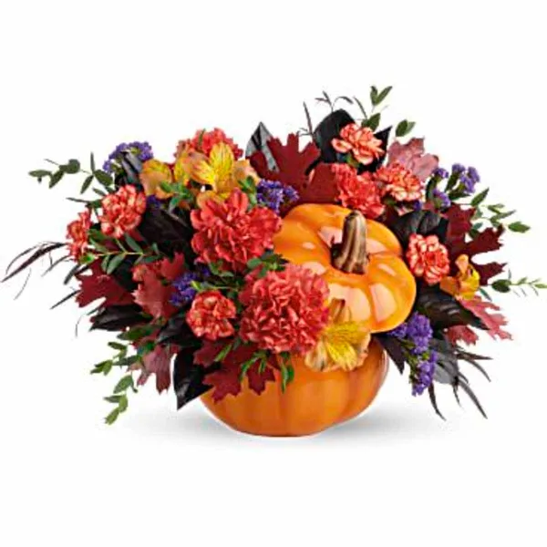 Autumn floral arrangement with red and orange carnations, alstroemeria, purple filler flowers, and dark foliage arranged around a ceramic pumpkin.
