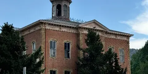 Exterior view of the Historic Chaffee County Courthouse, a red brick building with a distinctive dome and deer weathervane.