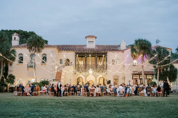 Outdoor wedding reception at a Spanish-style venue with string lights and seated guests.