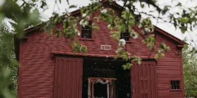 Exterior view of a red barn with the number 1830 on the front, set on a grassy lawn with trees in the foreground.
