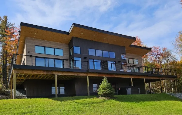 Exterior view of a modern two-story vacation rental home with a large deck and surrounding green lawn.