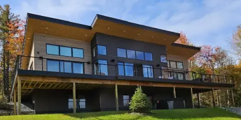 Exterior view of a modern two-story vacation rental home with a large deck and surrounding green lawn.