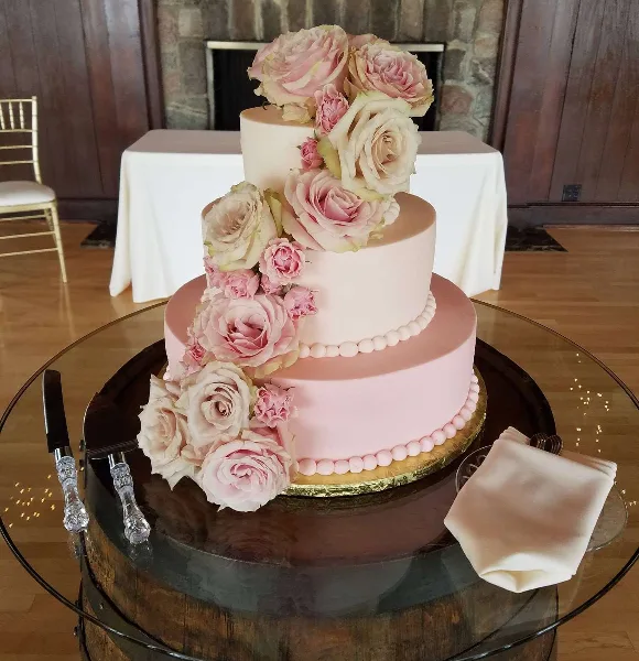 Three-tier pale pink wedding cake decorated with cascading pink and white flowers.