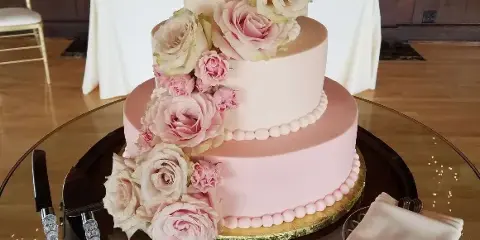 Three-tier pale pink wedding cake decorated with cascading pink and white flowers.