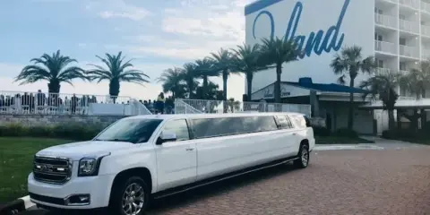 A white stretch limousine parked on a brick driveway in front of a coastal resort building with palm trees.