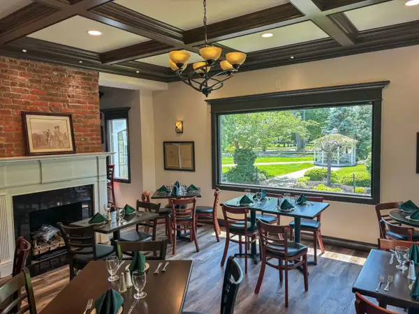 Interior view of the Claflin House dining room featuring a brick fireplace, wooden tables, and a large window overlooking a garden.