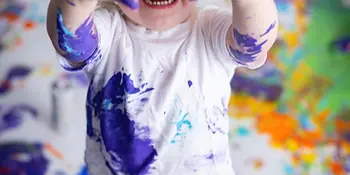 A young child with paint-covered hands and shirt smiling during a studio art photography session.