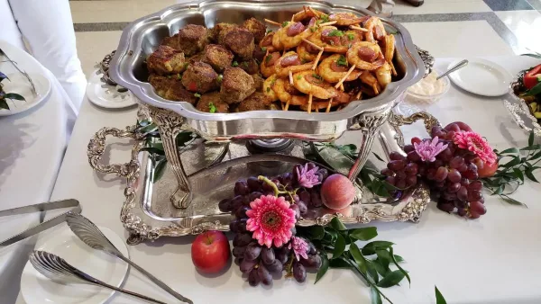 A silver chafing dish containing meatballs and shrimp garnished with flowers on a catering table.
