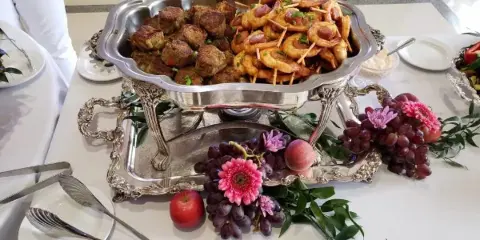 A silver chafing dish containing meatballs and shrimp garnished with flowers on a catering table.