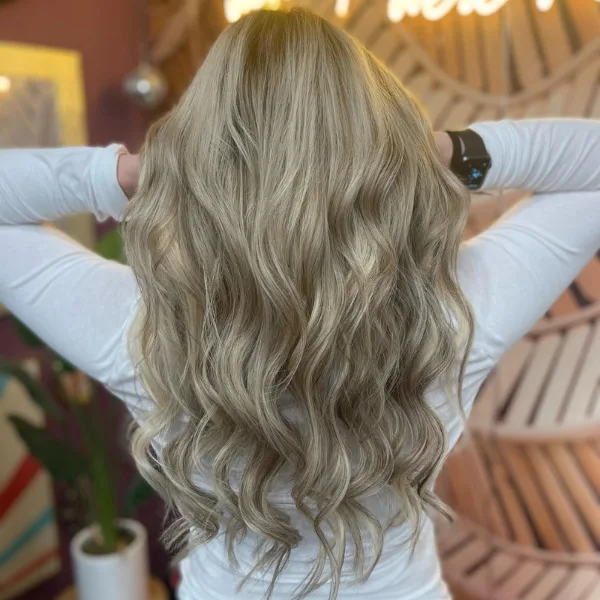 Back view of a client with long, wavy blonde hair in a salon.