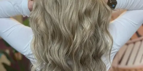 Back view of a client with long, wavy blonde hair in a salon.