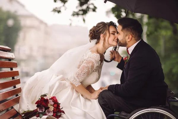 Bride and groom sharing a moment on a bench with a bouquet of red and pink roses