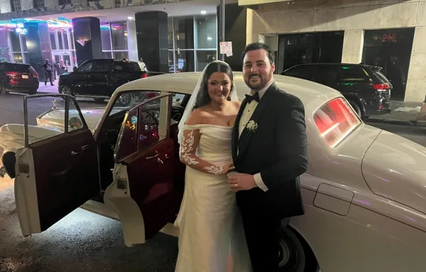 A bride and groom standing next to a vintage Rolls Royce car at night.
