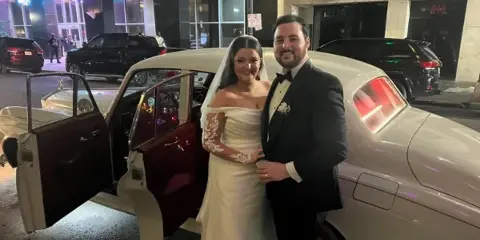 A bride and groom standing next to a vintage Rolls Royce car at night.